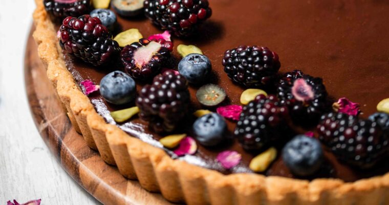 close up of blackberry rose ganache tart with black berries blueberries and tose petals
